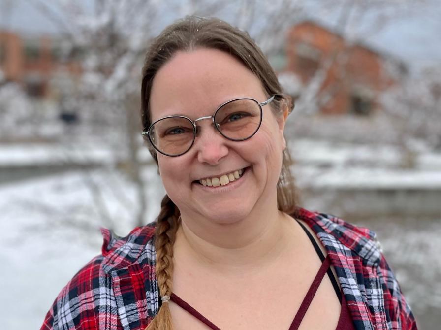 Bibliotekar Lisbeth Lohse Jørgensen. Hun smiler og er iført en rød bluse og skovmandsskjorte. Hun står udenfor, med sne i baggrunden.